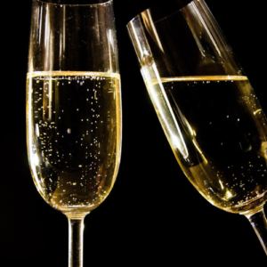 Dos copas de champán burbujeante chocando en un brindis, con fondo negro que resalta el brillo dorado de la bebida. Imagen elegante y festiva, perfecta para una invitación de boda o evento especial.