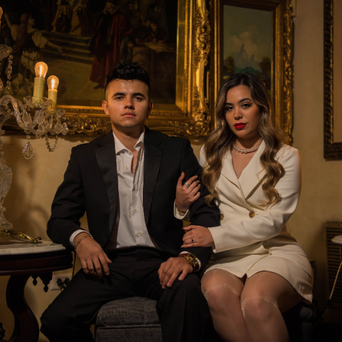 Pareja posando con elegancia en un entorno clásico y sofisticado, él con traje oscuro y ella con vestido blanco estilo minimalista. Escena íntima y refinada, ideal para una invitación de boda que combine elegancia moderna con un toque de sobriedad atemporal.